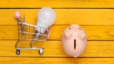 Saving electricity. Piggy bank-shaped shopping cart with LED bulbs and a yellow wooden surface. Flat.