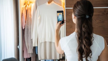 Young woman taking photos of old unwanted clothes for sale in smartphone app