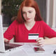 Serious freckled ginger woman uses laptop for e-commerce