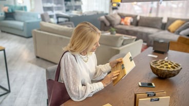 Choice, thought. Woman with a bag on her shoulder, holding wood samples for furniture in her hands, sitting at a table in a furniture showroom, choosing, serious.