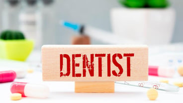 Dentist with plastic jaw model and mouth mirror on grey background