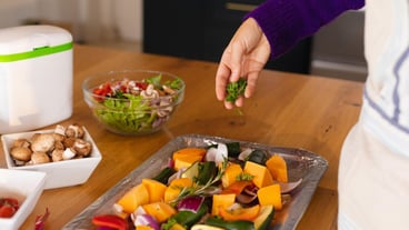 Midsection of caucasian woman standing in kitchen sprinkling fresh herbs on chopped vegetables. Domestic life, food and healthy eating, spending time alone at home.
