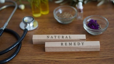 words NATURAL REMEDY written on wooden blocks on a table with herbs natural oils and a stethoscope