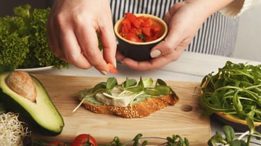 Cooking healthy vegetarian sandwiches. Female hands making whole grain bruschetta with avocado topping, juicy cherry tomatoes and microgreen. Eating right concept