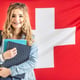 Student in braces smiles holding study material in from of flag of Switzerland.
