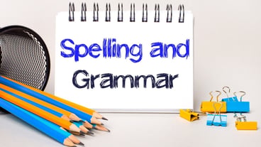 On a light background, yellow and blue pencils and paper clips and a white notebook with the text SPELLING AND GRAMMAR