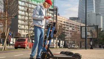Young guy chooses electric scooter rent in city activating with smartphone concept of modern urban t