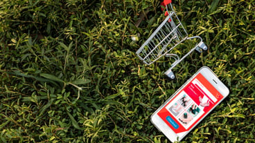 Smartphone and shopping cart on green grass. Shopping online or e-commerce concept on the website for environmentally.
