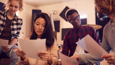 Portrait of multi-ethnic band writing music together, all holding lyric sheets