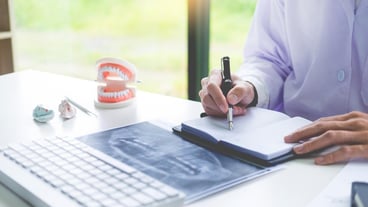 Midsection of dentist writing in book at office