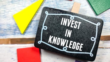 Business concept Text INVEST IN KNOWLEDGE on black board with colorful wooden puzzle on a wooden background