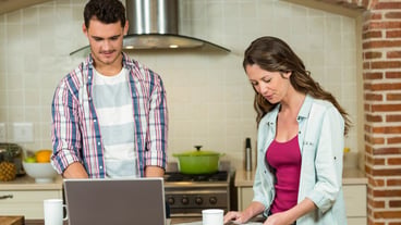Man using laptop and woman reading newspaper at kitchen counter