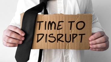 A disheveled business man holds up a cardboard sign with the words Time to disrupt