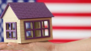 Small house with keys on hand against background of american flag