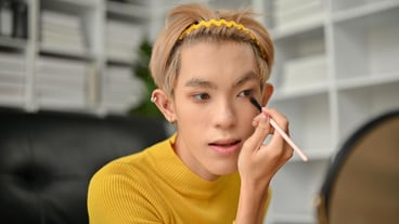 An attractive young Asian gay man is looking at the mirror and applying eyeshadow