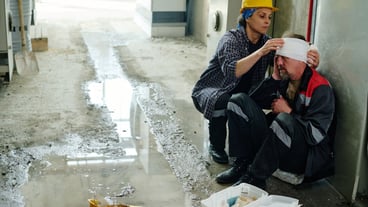 Worker receiving industrial injury in factory and colleague wrapping his injured head with bandage