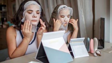 A girl and her mother apply a cosmetic face mask and play in front of the mirror, a home beauty salon.