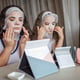 A girl and her mother apply a cosmetic face mask and play in front of the mirror, a home beauty salon.