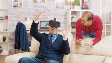 Nephew teaching his grandfather how to use virtual reality headset in living room.