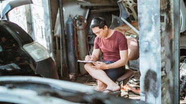 Young male mechanic sitting while writing a list of car repairs at a repair shop