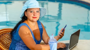 A young woman in a hat at a table in the morning by the pool with a smartphone and works remotely