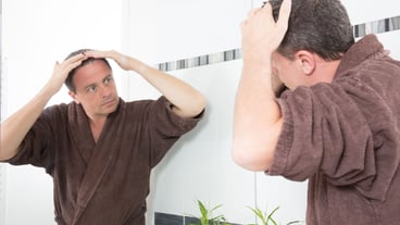 Man controls hair loss in the bathroom looking in a mirror and fixing his hair