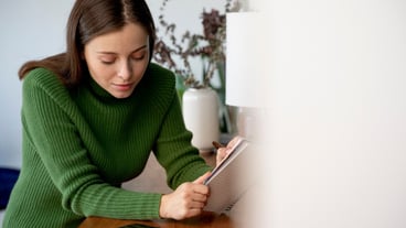 Woman writing something on a notebook while looking at her smartphone