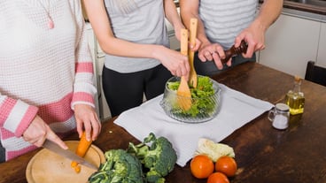 Close-up of friends preparing a fresh vegetable salad at a wooden table