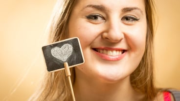 Happy woman posing with a small board on which a heart is drawn