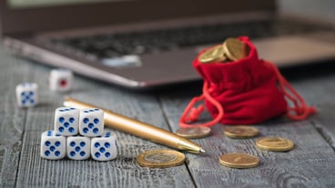 dice and a pile of coins in front of a laptop with business schedules.