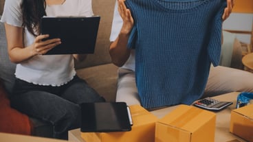 Two Asian blogger showing clothes in front of the camera to recording vlog video live streaming at her shop Online Shopping Cart notion on sofa at home