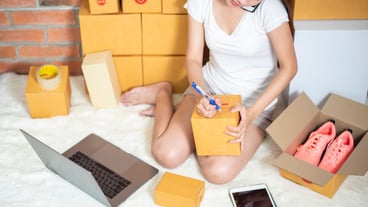 Woman entrepreneur owner SME business is checking order with smartphone, laptop and packaging box to send her customer