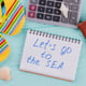 Travel planning concept at office with passports, sandals and calculator. Let's go to the sea written on notepad.