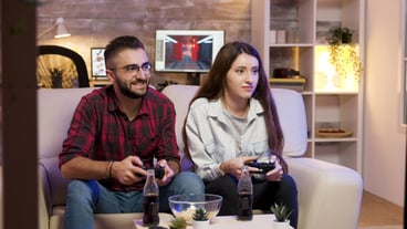 Joyful young couple sitting on the couple and playing video games on television using controllers.