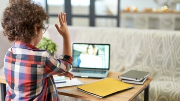Rear view of latin school boy raising his hand during online lesson via video chat app. Child using laptop while studying at home. Online education, technology, homeschooling. Selective focus