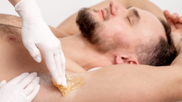Cosmetologist applying wax paste on male armpit