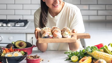 A young woman with spring rolls in rice paper in the kitchen