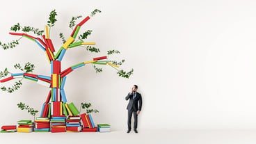 A man looking at a colorful tree sculpture made of books with green leaves set against a white backg