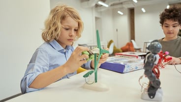 Create things caucasian boy examining technical toy caucasian boy while sitting at the table together with other