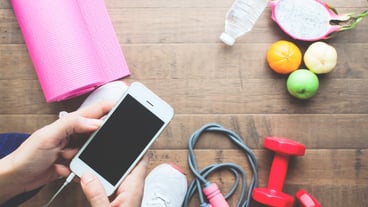 Overhead view of fitness woman with cell phone, sports equipment and fruit on wooden floor, healthy lifestyle concept