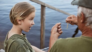 Little boy fishing with his dad, being astonished because of tangled line on fishing rod, family posing on wooden stairs leading to water, surprised male child.