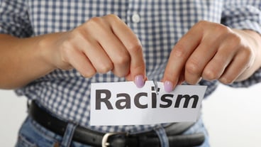 Woman tearing up paper sheet with word Racism on white background closeup