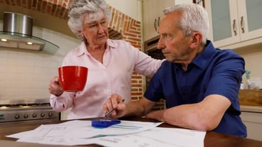 Senior caucasian couple spending time at home together, sitting in kitchen, the man looking at paperwork and the woman holding a cup. isolating during coronavirus covid 19 quarantine lockdown.