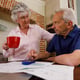 Senior caucasian couple spending time at home together, sitting in kitchen, the man looking at paperwork and the woman holding a cup. isolating during coronavirus covid 19 quarantine lockdown.
