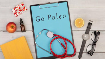 Medecine and diet concept clipboard with text Go Paleo pills fruits stethoscope book eyeglasses