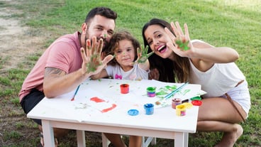 Parents with daughter showing messy hands while painting in the park