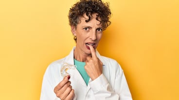 Doctor with invisible dental aligner on yellow relaxed thinking about something