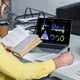 bearded man studying with book near laptop with charts and graphs on screen in modern office