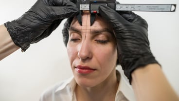 Eyebrow shaping stylist measures eyebrows with a ruler. Beautician measures a gorgeous brunette woman's eyebrows before permanent eyebrow makeup in a cosmetology salon.