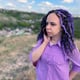 Young beautiful woman talking on mobile phone standing in hilly terrain Cute vivid female with dreadlocks speaking on smartphone standing outdoors in cloudy windy summer weather